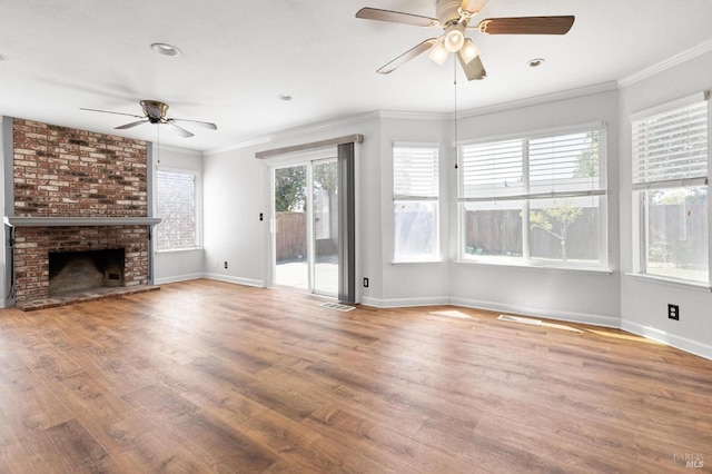 unfurnished living room with wood finished floors, a brick fireplace, baseboards, a ceiling fan, and crown molding