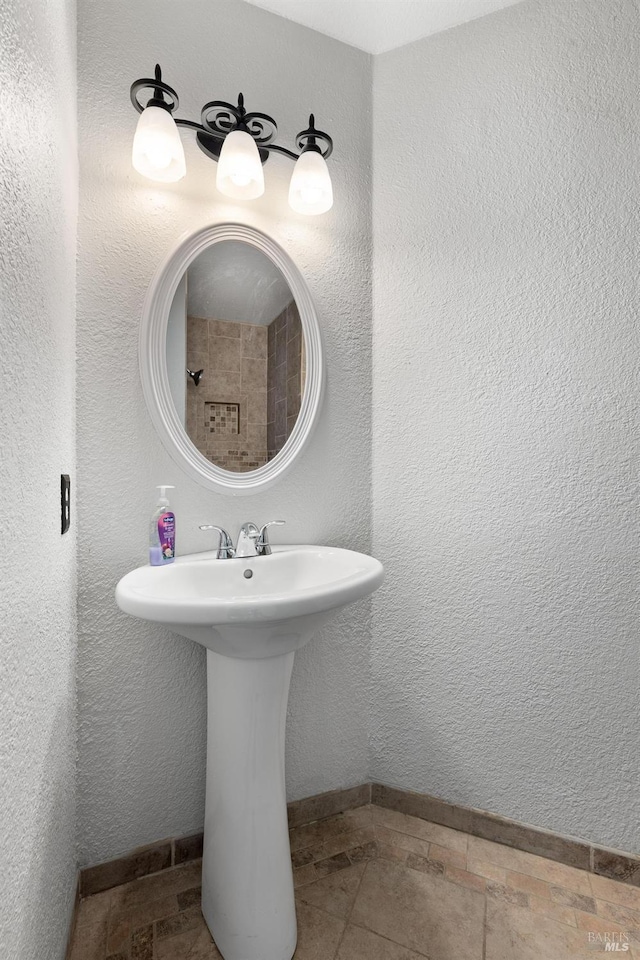 bathroom with baseboards, stone tile flooring, and a sink