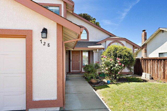 property entrance featuring stucco siding, a yard, fence, roof with shingles, and an attached garage