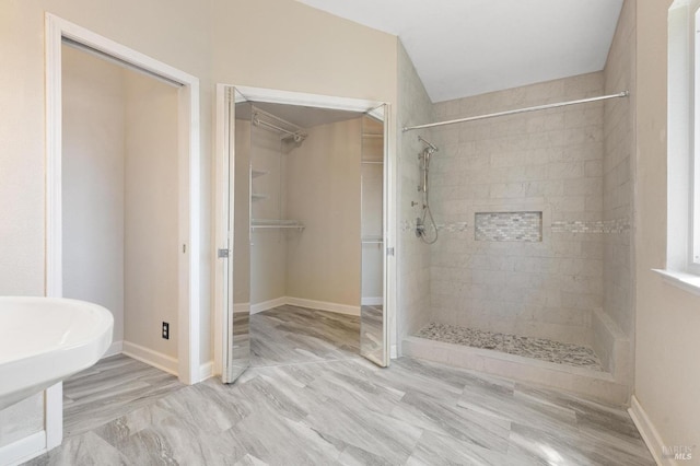 bathroom featuring a tile shower, baseboards, and a spacious closet