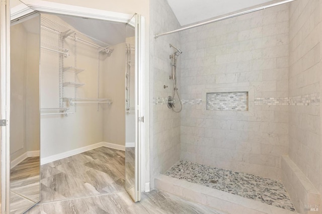 full bathroom with a tile shower, baseboards, and a spacious closet