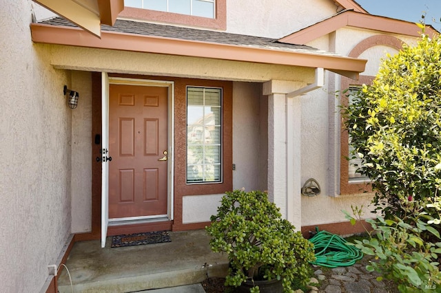 view of exterior entry featuring a shingled roof and stucco siding