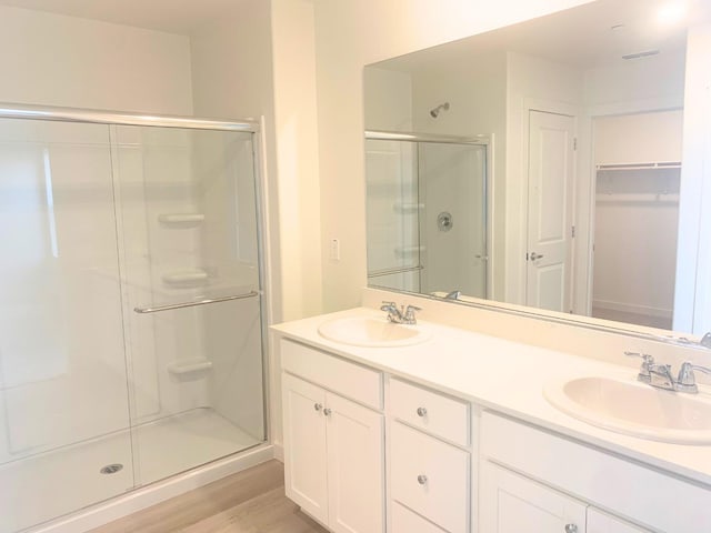 bathroom with a stall shower, double vanity, a sink, and wood finished floors