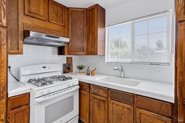 kitchen with tasteful backsplash, a sink, under cabinet range hood, gas range gas stove, and tile countertops