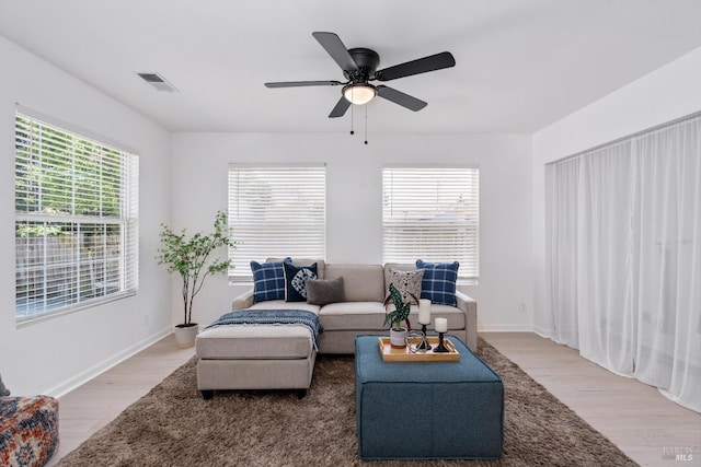 living area featuring a ceiling fan, visible vents, a healthy amount of sunlight, and light wood-type flooring