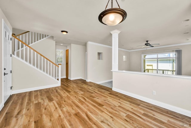 unfurnished living room featuring stairway, baseboards, light wood-type flooring, ornate columns, and a ceiling fan