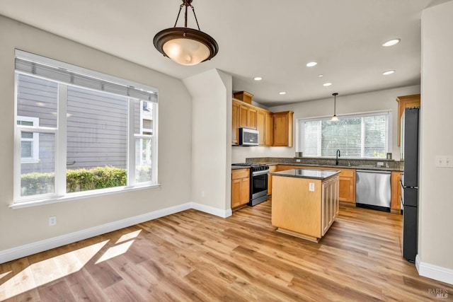 kitchen featuring light wood-style flooring, appliances with stainless steel finishes, dark countertops, a sink, and baseboards