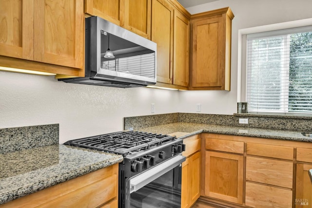 kitchen with stainless steel microwave, light stone countertops, and gas range