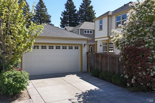 traditional home featuring fence, concrete driveway, a shingled roof, and a garage
