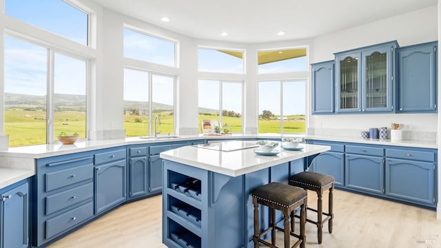 kitchen with a sink, light wood-style floors, a breakfast bar, a kitchen island, and blue cabinetry