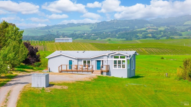 back of property with a rural view, stucco siding, a deck with mountain view, driveway, and a lawn