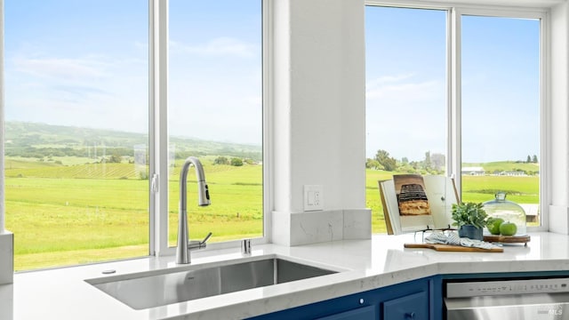 kitchen with a sink, a rural view, a healthy amount of sunlight, dishwasher, and blue cabinets