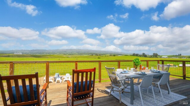deck featuring a rural view, outdoor dining area, and a yard