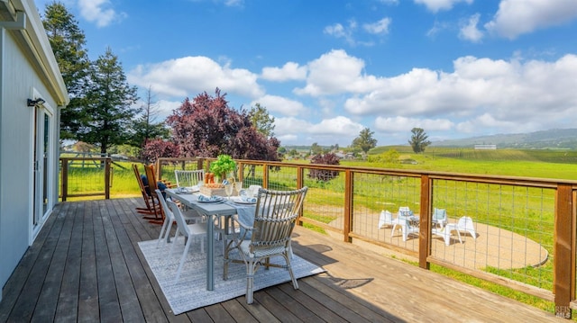 wooden deck with a lawn, a rural view, and outdoor dining space