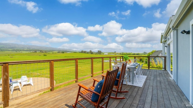 wooden deck featuring a lawn, outdoor dining area, and a rural view