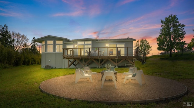 back of house at dusk with a lawn and a wooden deck