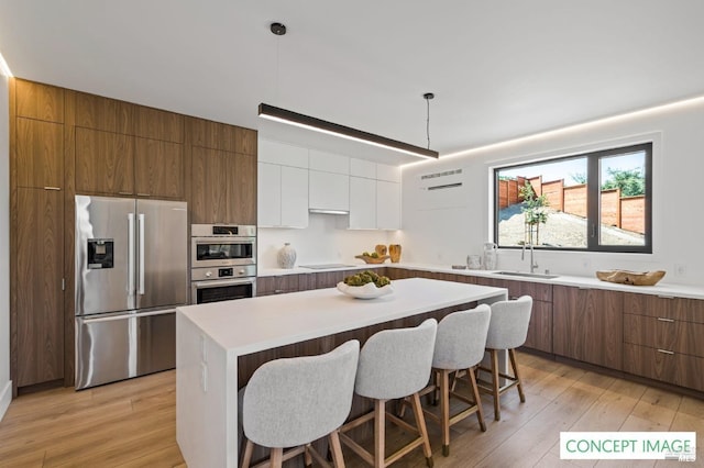 kitchen featuring a kitchen breakfast bar, white cabinetry, light wood-style flooring, a sink, and stainless steel appliances