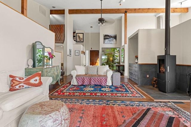living room featuring wood finished floors, beamed ceiling, visible vents, a wood stove, and a towering ceiling