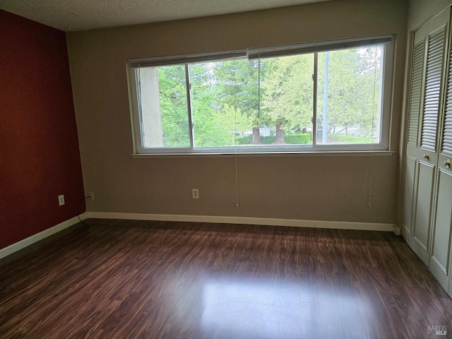 unfurnished room featuring dark wood-type flooring, a healthy amount of sunlight, and baseboards