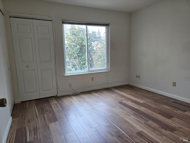 unfurnished bedroom with a closet, multiple windows, wood finished floors, and baseboards