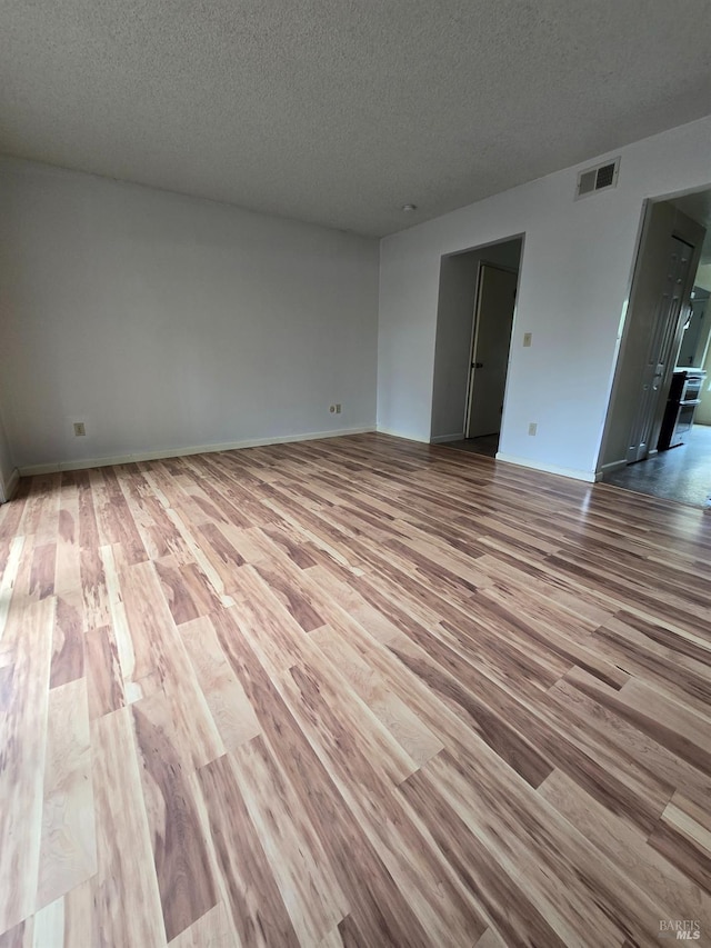 spare room with baseboards, visible vents, wood finished floors, and a textured ceiling