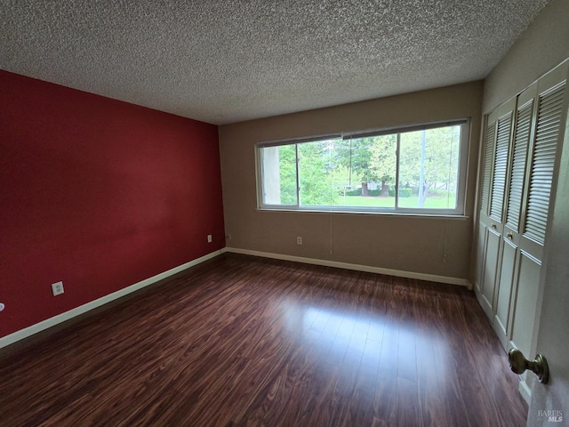empty room featuring baseboards, a textured ceiling, and dark wood-style flooring