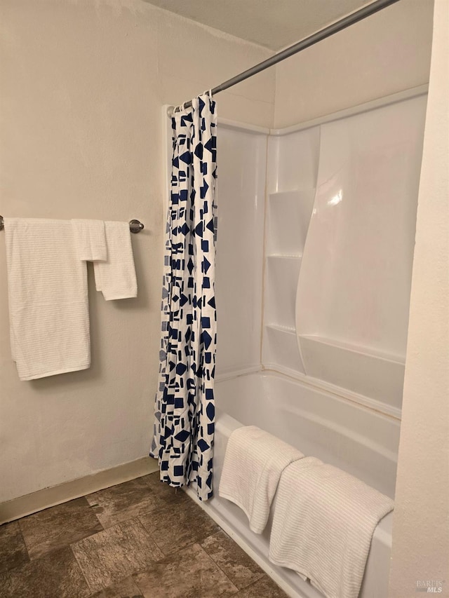 full bathroom with shower / bathtub combination with curtain, stone finish floor, and baseboards