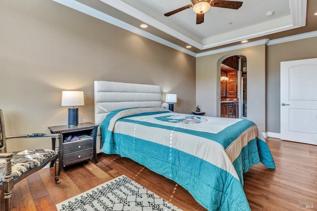 bedroom with recessed lighting, a tray ceiling, ornamental molding, arched walkways, and wood finished floors