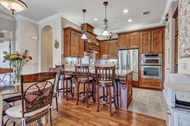 kitchen featuring visible vents, stainless steel appliances, arched walkways, and brown cabinetry
