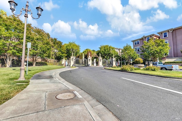 view of street with a gated entry, curbs, and sidewalks