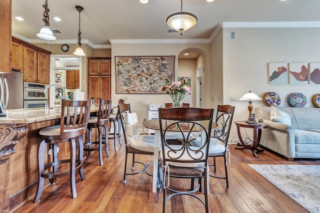 dining room with visible vents, crown molding, light wood-style flooring, and arched walkways