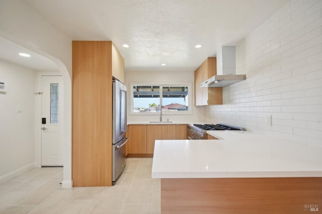 kitchen featuring stainless steel appliances, light countertops, wall chimney exhaust hood, modern cabinets, and a peninsula