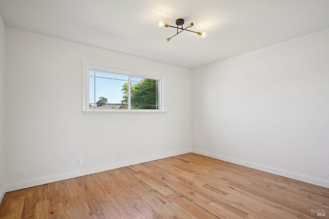 unfurnished room featuring an inviting chandelier, baseboards, and light wood-type flooring