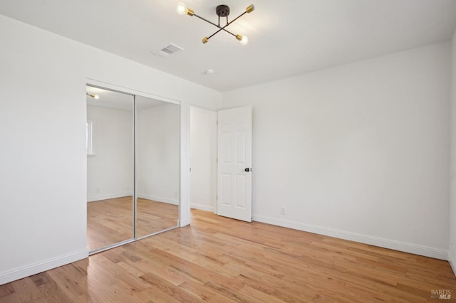 unfurnished bedroom with wood finished floors, a chandelier, a closet, baseboards, and visible vents