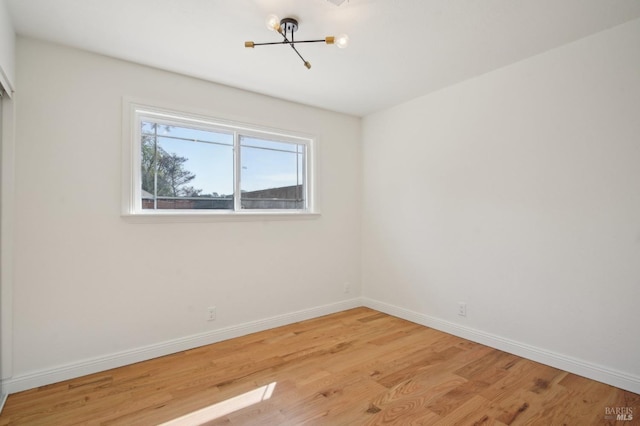 spare room featuring baseboards, a chandelier, and light wood-type flooring