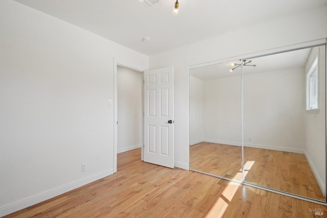 unfurnished bedroom featuring a closet, an inviting chandelier, wood finished floors, and baseboards