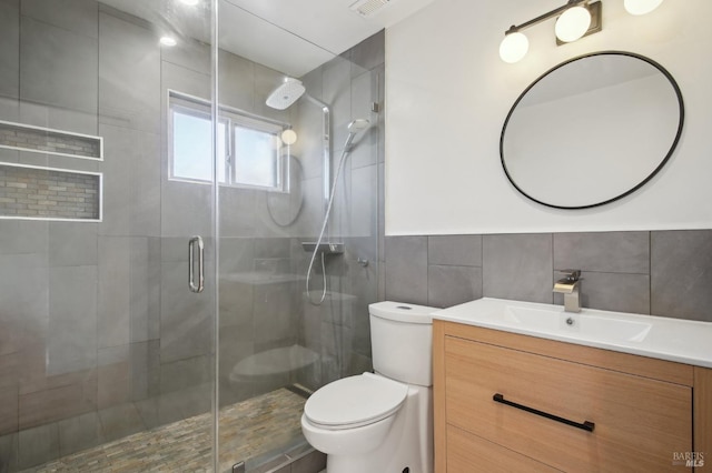bathroom featuring vanity, toilet, a shower stall, and tile walls