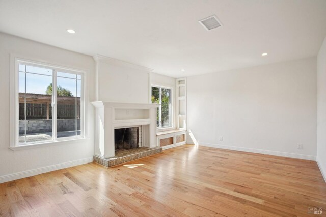 unfurnished living room featuring baseboards, light wood-type flooring, a fireplace with raised hearth, and plenty of natural light