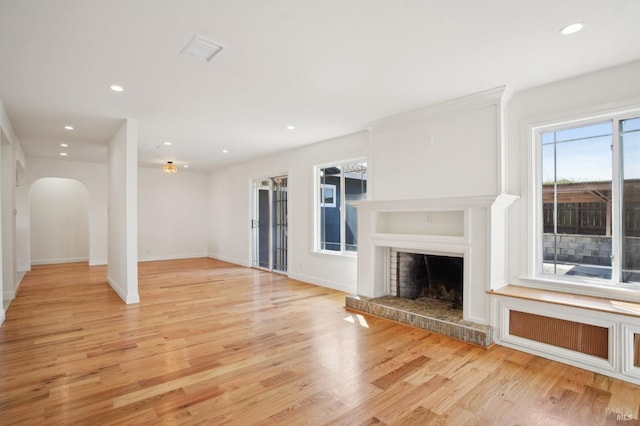 unfurnished living room with recessed lighting, arched walkways, light wood-style flooring, a fireplace with raised hearth, and baseboards