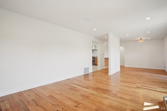 empty room with light wood-style flooring, visible vents, baseboards, arched walkways, and recessed lighting