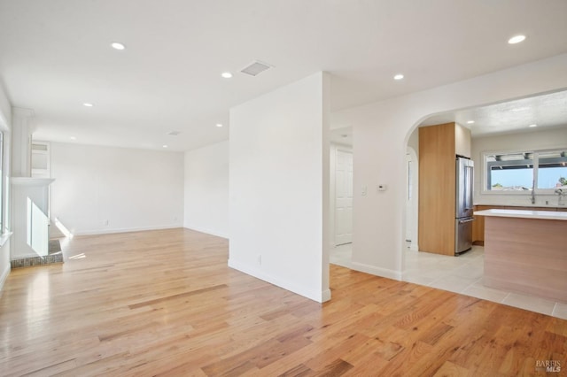 unfurnished living room with baseboards, recessed lighting, arched walkways, and light wood finished floors