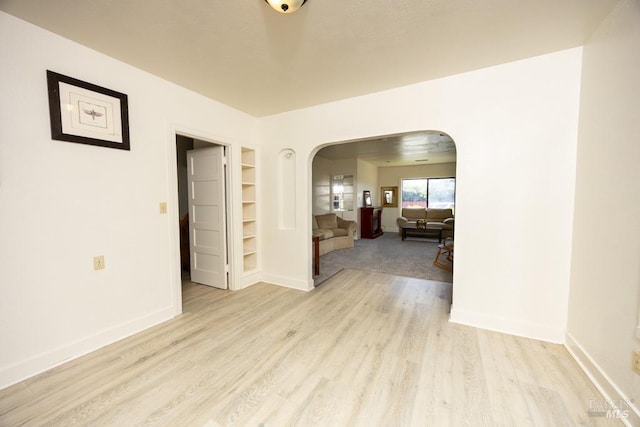unfurnished room featuring baseboards, arched walkways, light wood-style floors, and built in features