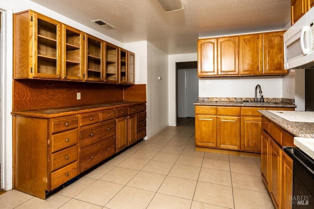 kitchen featuring visible vents, white microwave, brown cabinetry, and a sink