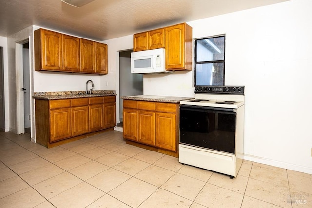 kitchen with a sink, range with electric cooktop, light tile patterned flooring, brown cabinetry, and white microwave