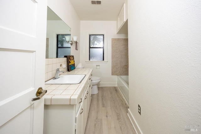 bathroom featuring vanity, tasteful backsplash, toilet, visible vents, and wood finished floors
