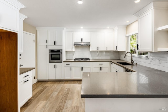 kitchen featuring white cabinetry, a sink, appliances with stainless steel finishes, under cabinet range hood, and light wood finished floors