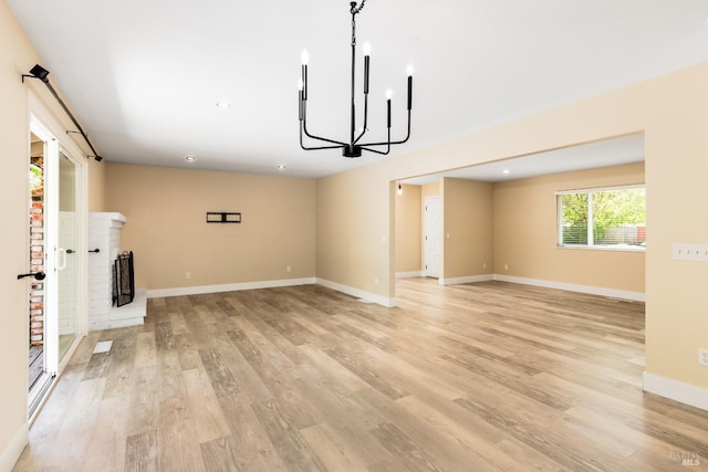 unfurnished living room featuring recessed lighting, a chandelier, a fireplace, light wood-style floors, and baseboards