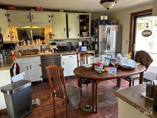 kitchen featuring open shelves, stainless steel appliances, brick patterned floor, and a sink