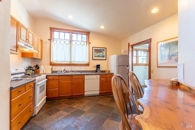 kitchen with white appliances, under cabinet range hood, stone finish flooring, a sink, and lofted ceiling