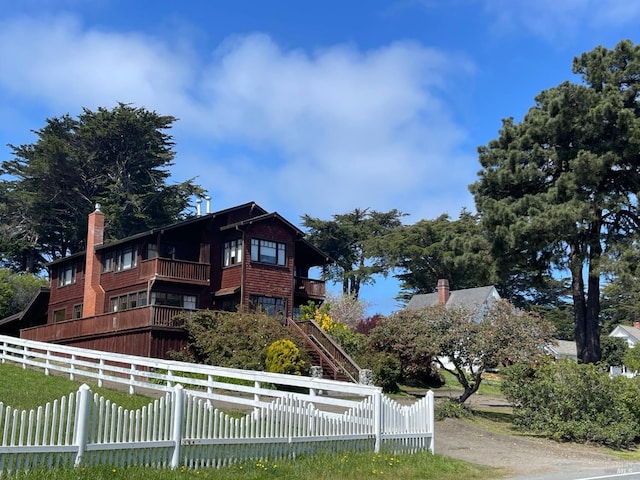 view of front of house with a balcony, a fenced front yard, and a chimney